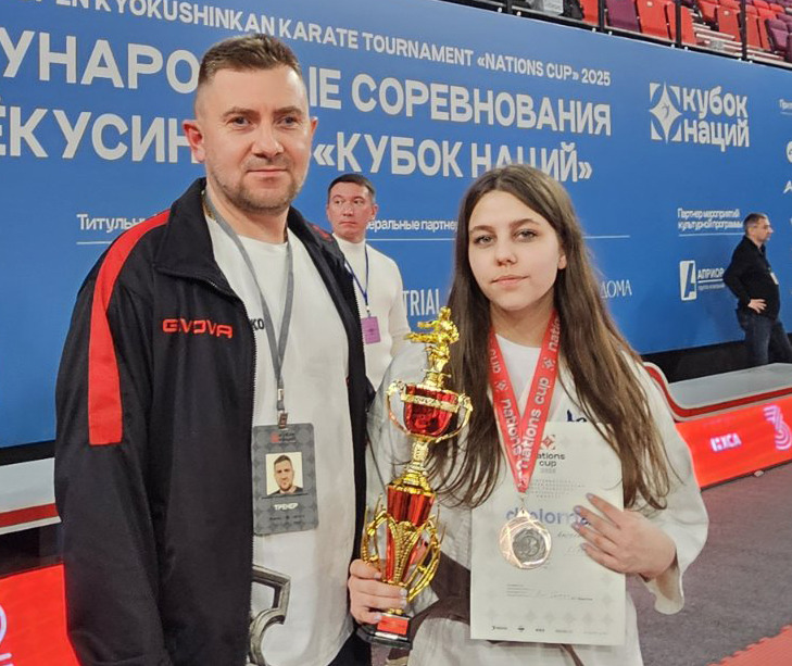 Справа на лево: С кубком и медалью Ангелина Ходарцевич, 1 дан, чёрный пояс. «Кубок Наций», Москва, 3-е место, 2025. Тренер Семашко Андрей Владимирович (клуб “С-4 додзё”, Лида).