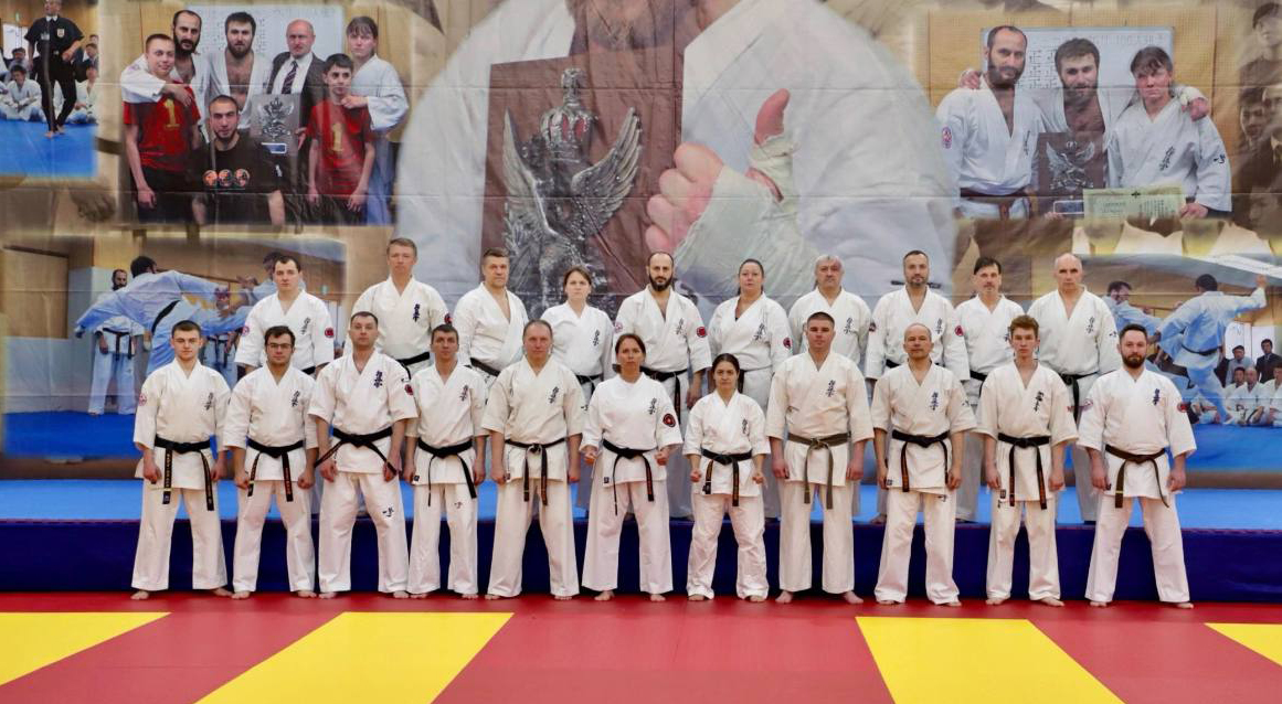 21 каратист с черными поясами боевого марафона 100 боёв «Стремись быть лучше» стоят на фоне банера. Москва.