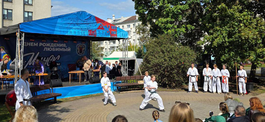 Киокушиновцы разных возрастов перед уличной сценой. Три спортсменки демонстрируют ката